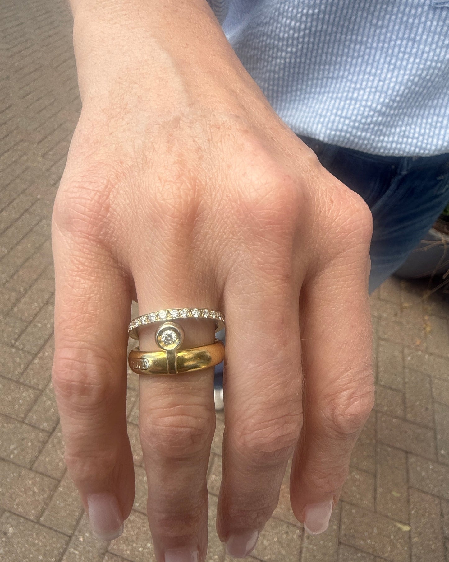 Hand wearing a gold ring with a diamond on a paved surface