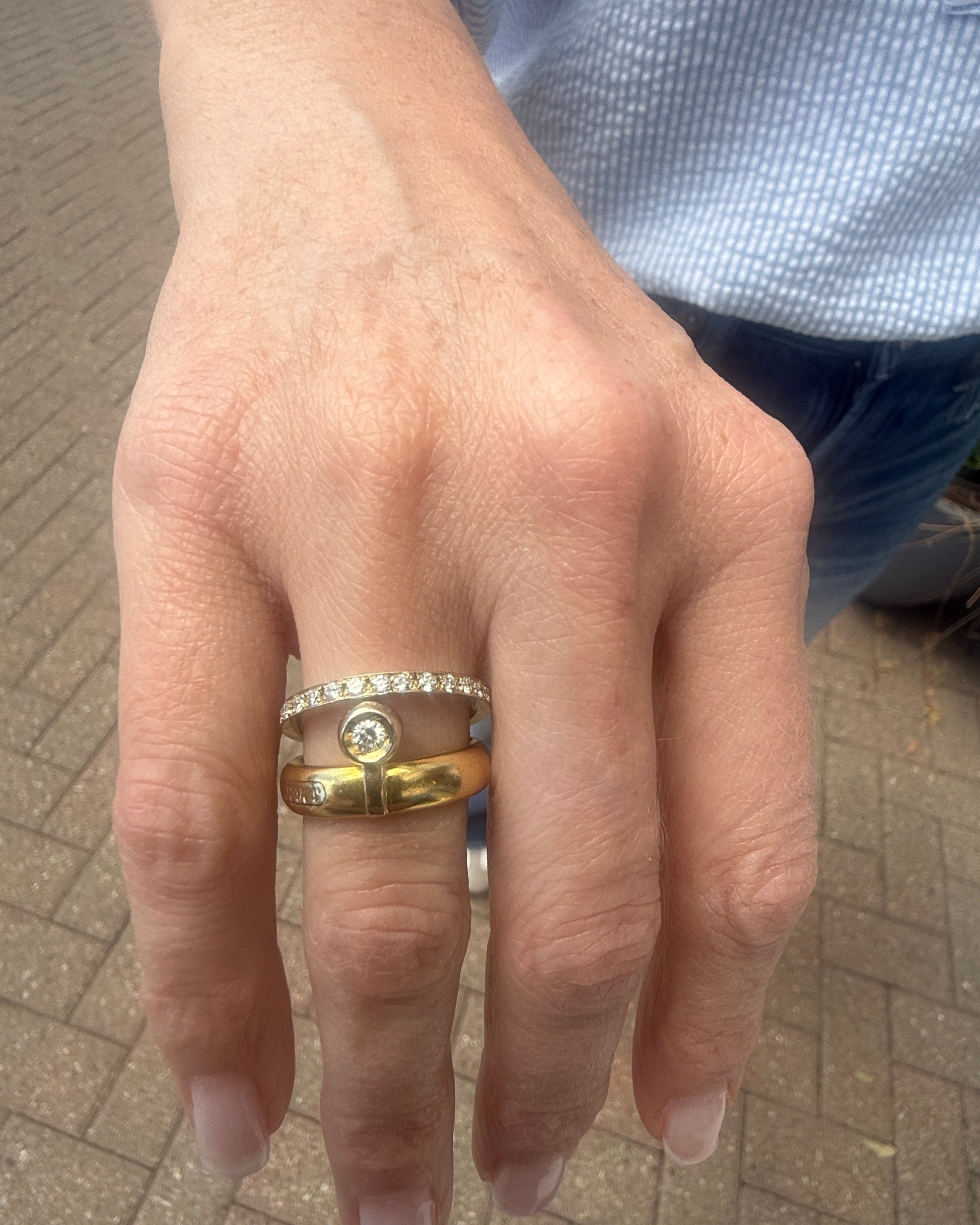 Hand wearing a gold ring with a diamond on a paved surface