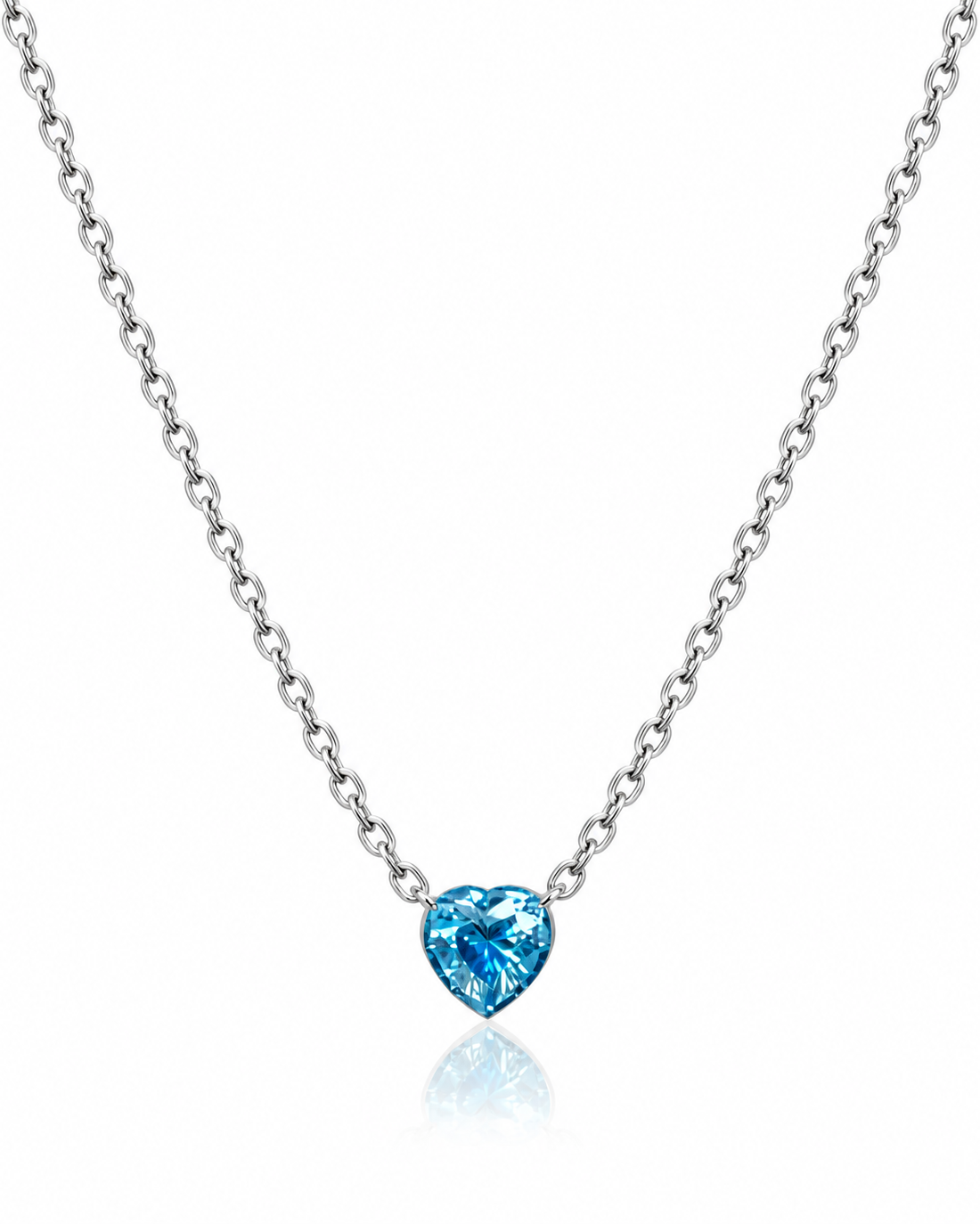 A silver chain necklace with a heart-shaped blue gemstone pendant, displayed against a clean white background with a soft reflection below.
