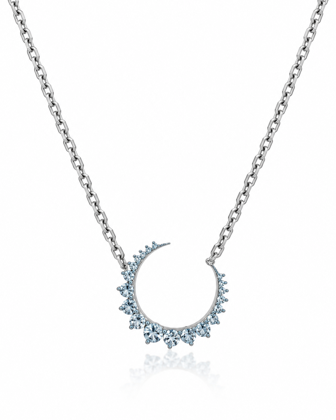 A silver-toned chain necklace featuring a crescent moon pendant adorned with small light blue gemstones, shown on a clean white background with a subtle reflection below.