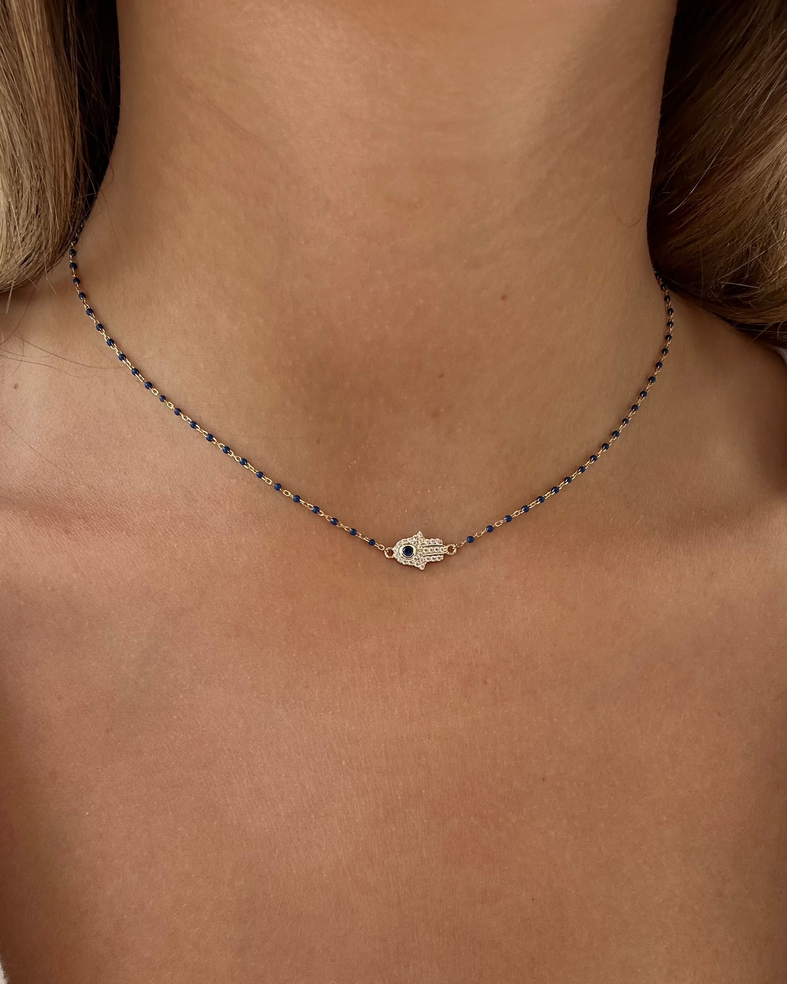 A close-up of a neck wearing the GAGA Hamsa Enamel Necklace by Dylan James Jewelry, featuring a small hand pendant on a fine gold-plated sterling silver chain.