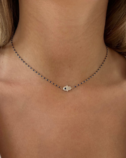 A close-up of a neck wearing the GAGA Hamsa Enamel Necklace by Dylan James Jewelry, featuring a small hand pendant on a fine gold-plated sterling silver chain.