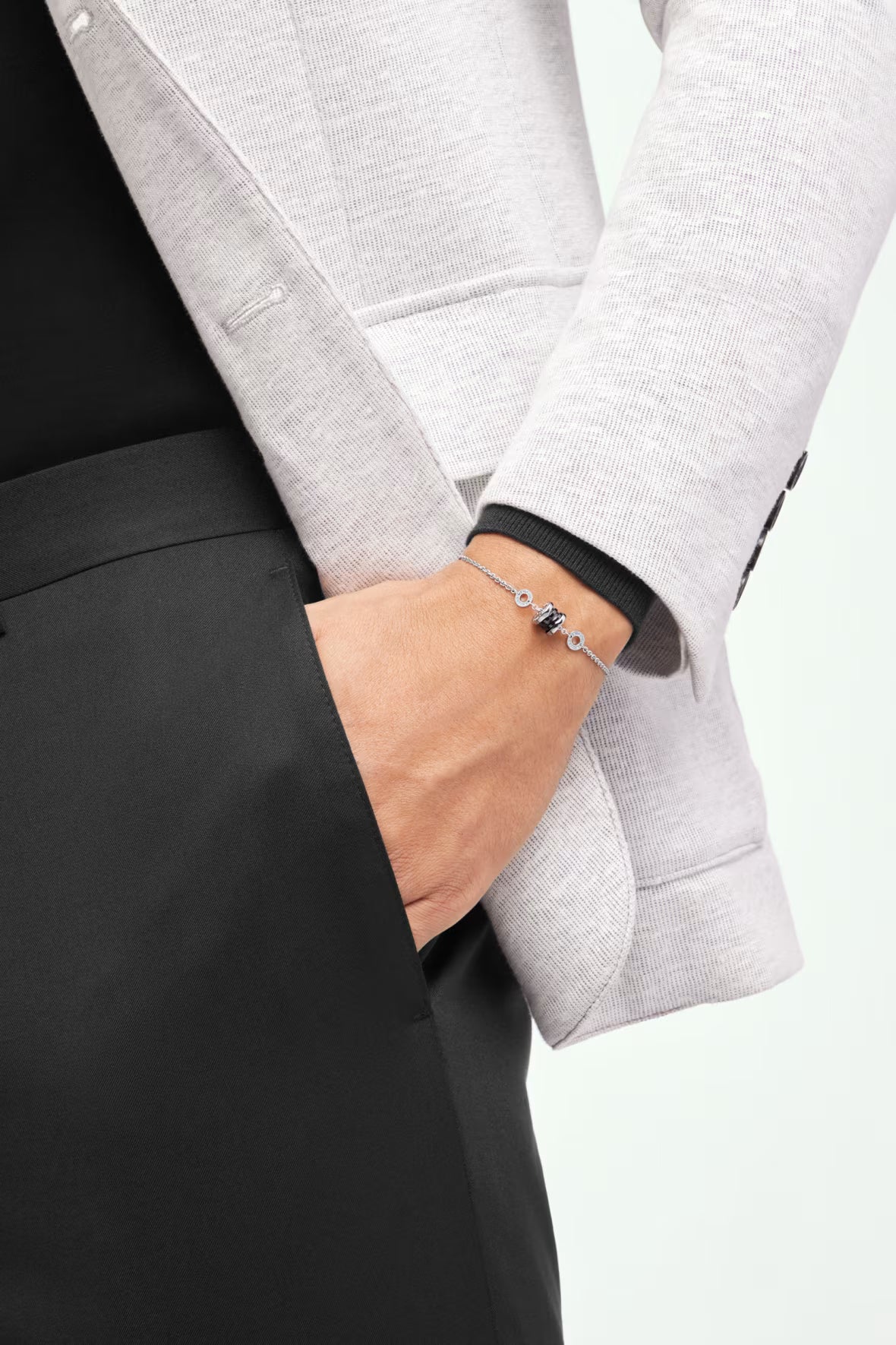 Person wearing a gray jacket and black pants with a bracelet on a white background