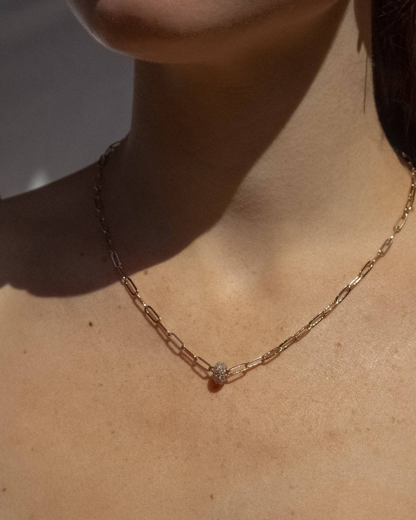 Gold chain necklace with a small pendant on a person's neck against a neutral background