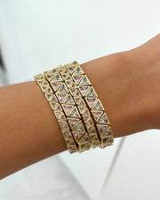 A close-up of a person's wrist wearing a stack of gold-toned pyramid-link bracelets with small pink gemstone accents.