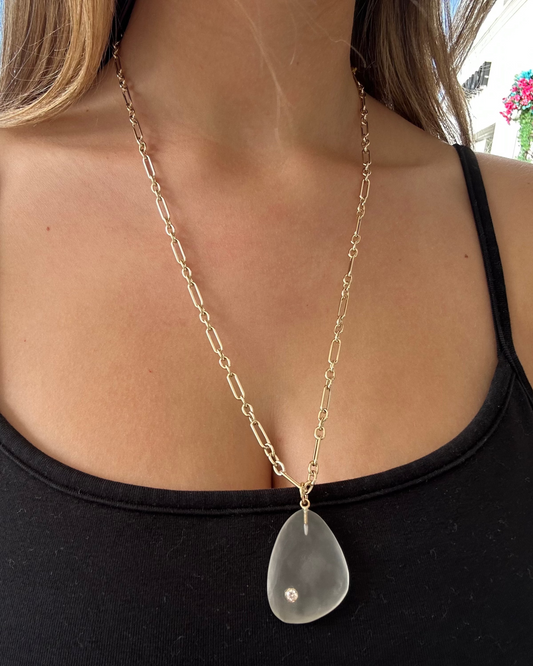 Gold chain necklace with a clear pendant worn by a person outdoors.