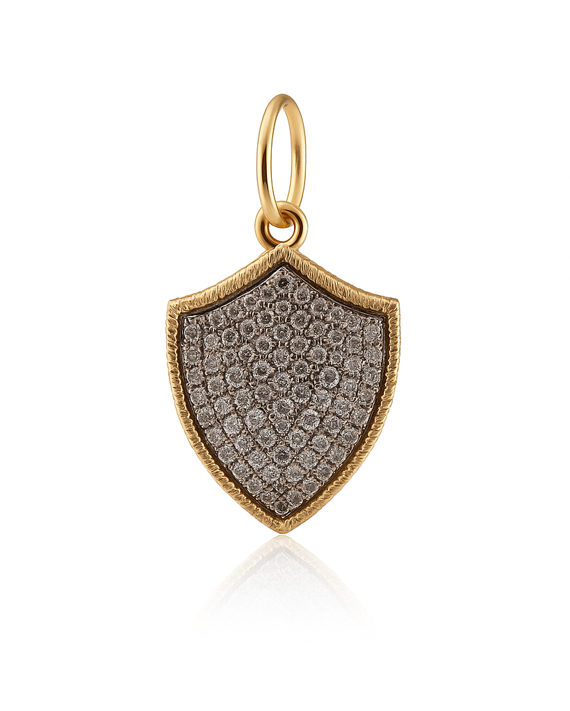 A shield-shaped pendant charm in yellow gold, featuring a textured pavé setting with small clear stones that appear silver-toned, set against a clean white background with a soft reflection.