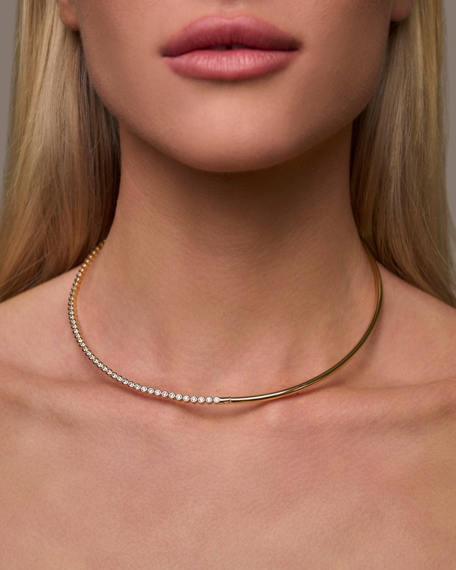 Close-up of a person wearing a gold necklace against a neutral background