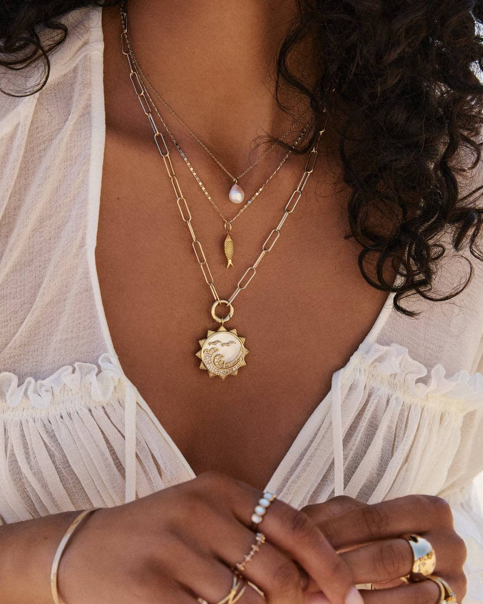 Close-up of a person wearing multiple gold necklaces and rings with a blurred background