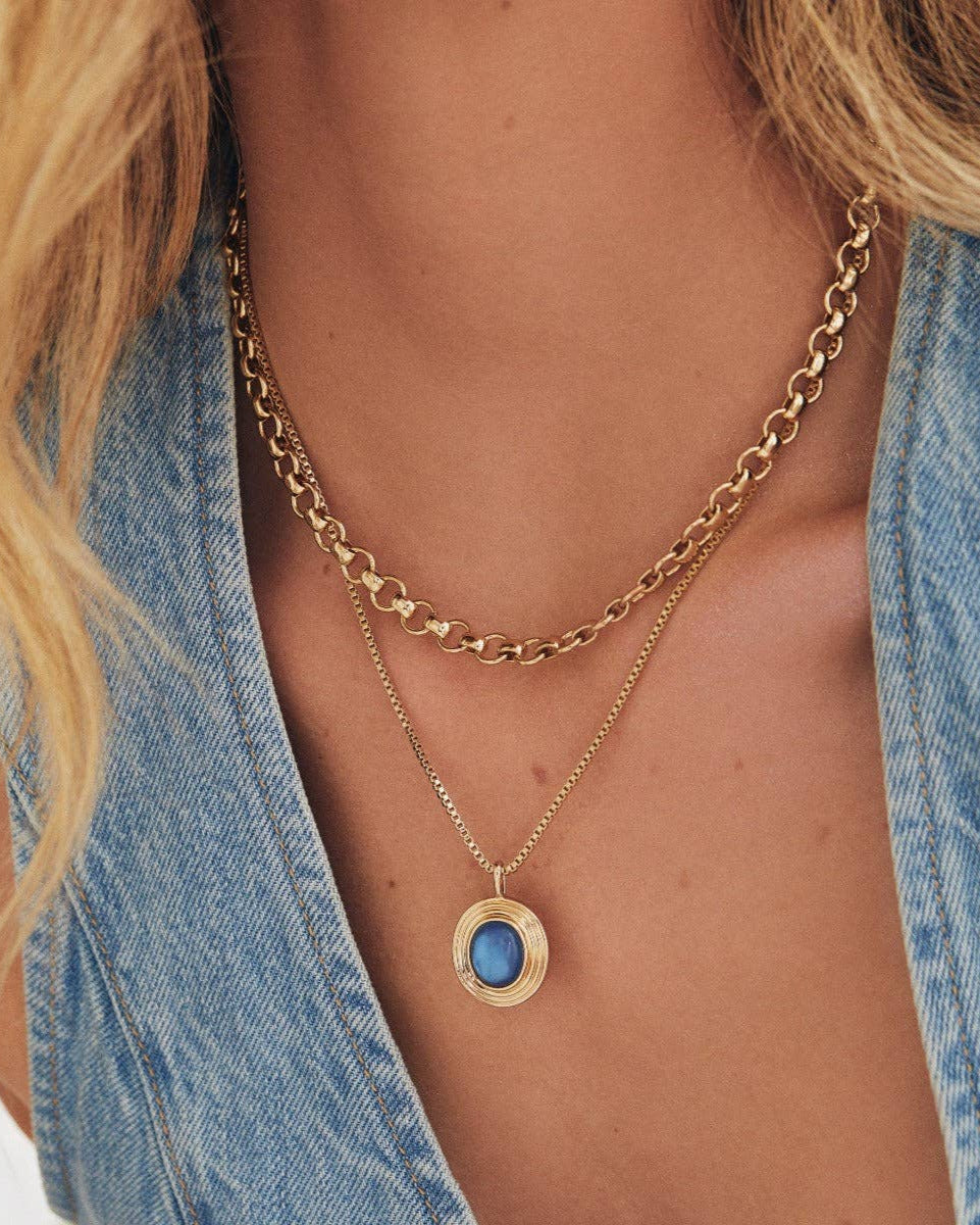 A woman in a sleeveless blue denim top wears the Elizabeth Stone Jewelry Venus Chain - Petite, a 14k gold-plated necklace, styled with a petite chain and blue stone pendant.