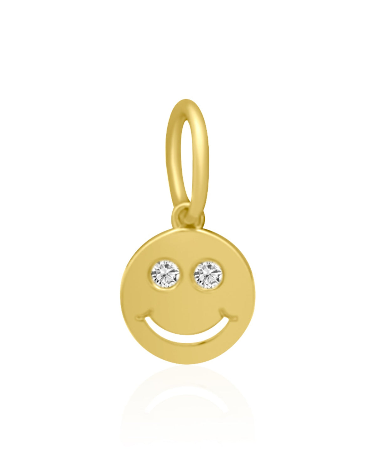 A gold smiley face charm pendant with two small clear gemstone eyes, shown on a clean white background with a soft reflection below.