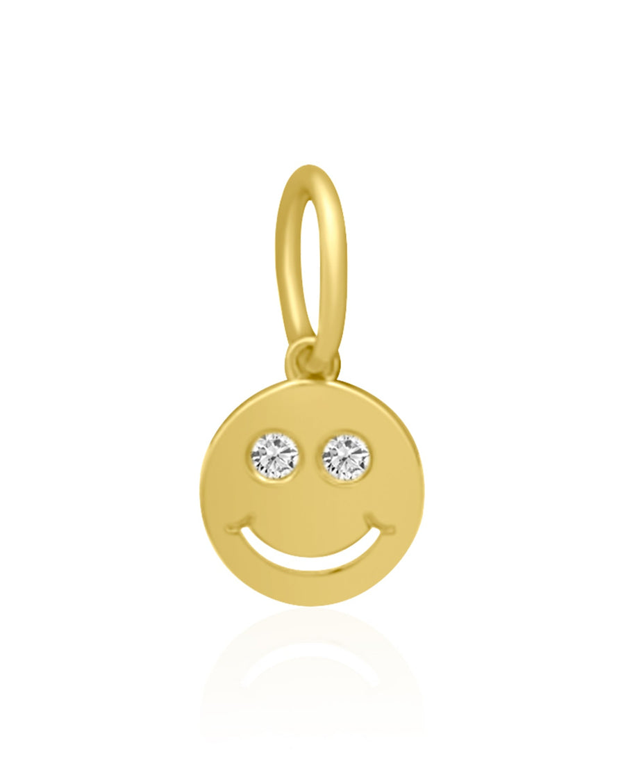 A gold smiley face charm pendant with two small clear gemstone eyes, shown on a clean white background with a soft reflection below.