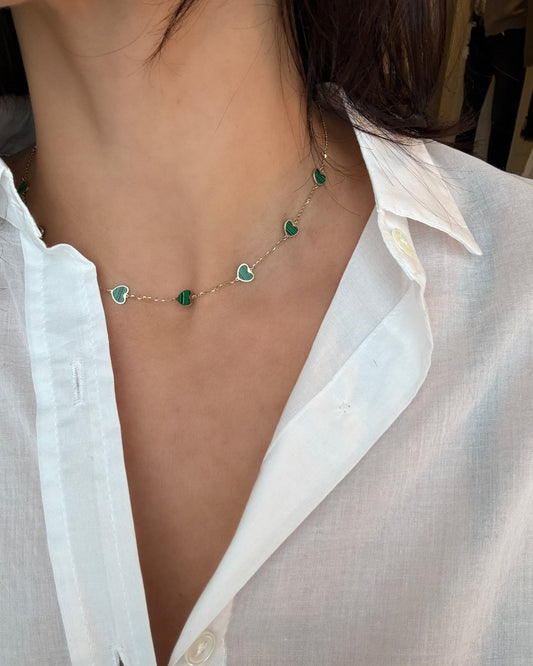 Person wearing a delicate necklace with green heart-shaped pendants on a white shirt.