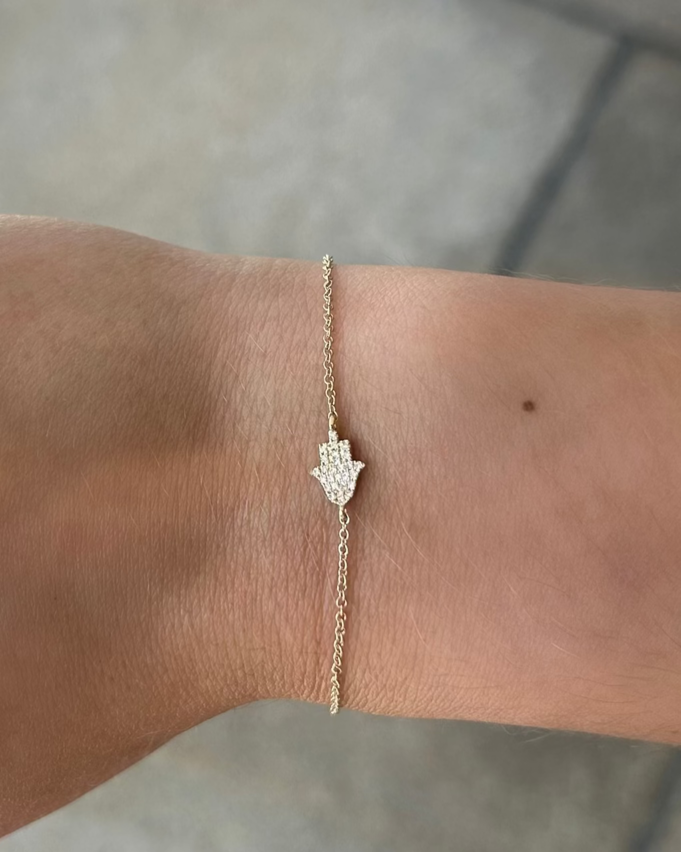 Gold bracelet with a hamsa hand design on a wrist against a neutral background