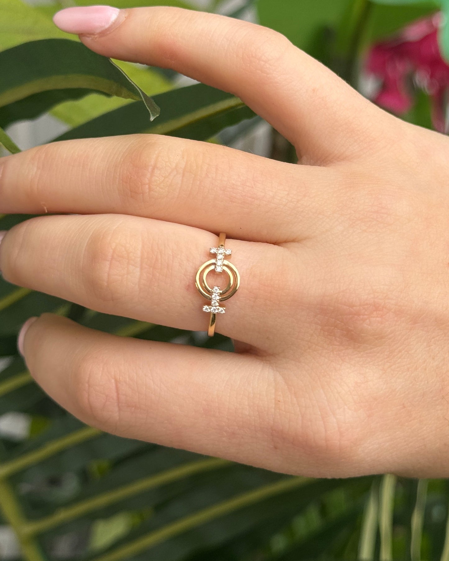 Hand wearing a gold ring with a green leafy background