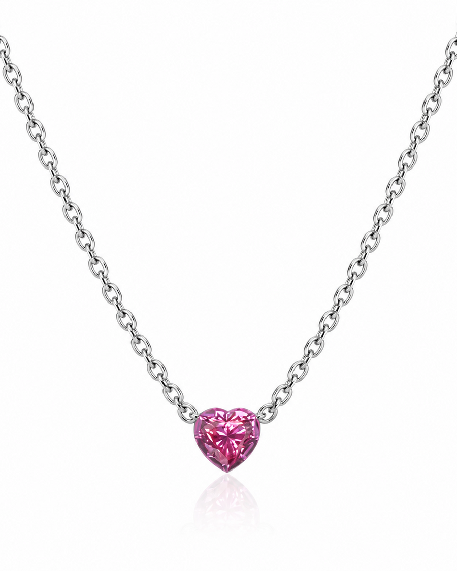 A silver chain necklace featuring a small, heart-shaped pink gemstone pendant, displayed against a clean white background with a subtle reflection below.