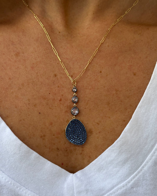 Necklace with a blue pendant on a person's neck against a white shirt.