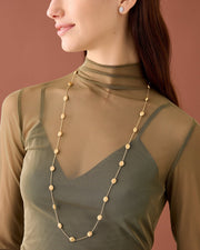 Woman wearing a long gold necklace against a brown background