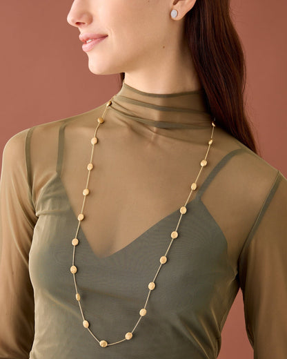Woman wearing a long gold necklace against a brown background