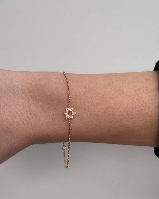 The NOAH Diamond Bracelet by Dylan James Jewelry features a star-shaped charm in 14kt gold, accented with shimmering diamonds, elegantly worn on a person's wrist against a neutral background.