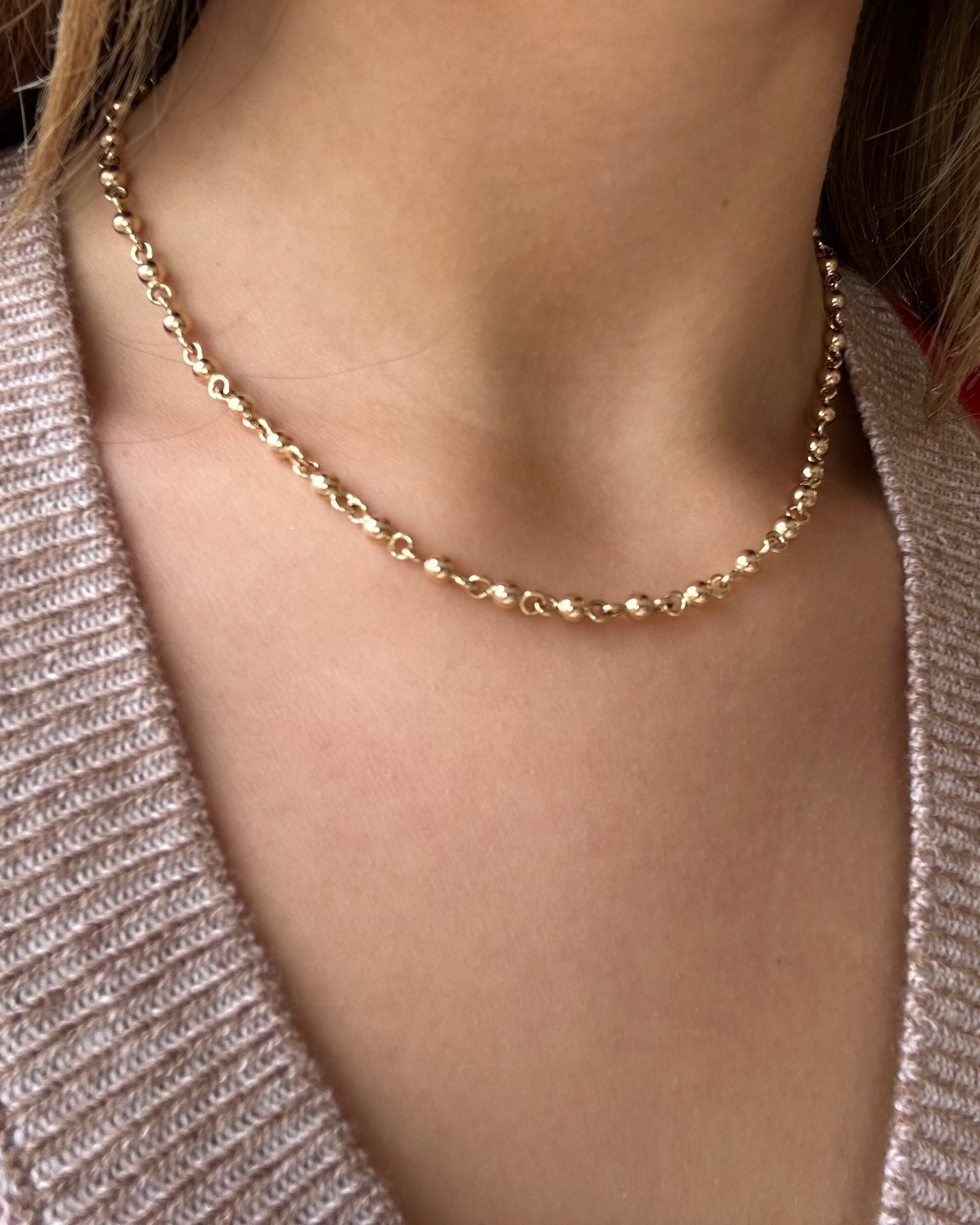 Gold necklace worn by a person with a patterned cardigan