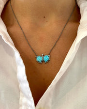 A close-up of a person wearing a white collared shirt and the DYLANJAMES BLAIR Butterfly Necklace, adorned with diamonds and delicate turquoise accents.