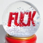 The artware FUCK Snowglobe features bold red "FUCK" lettering inside a glass globe, surrounded by swirling white snow-like particles.